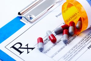 Red and White pills rolling out of an orange prescription bottle on top of a prescription pad